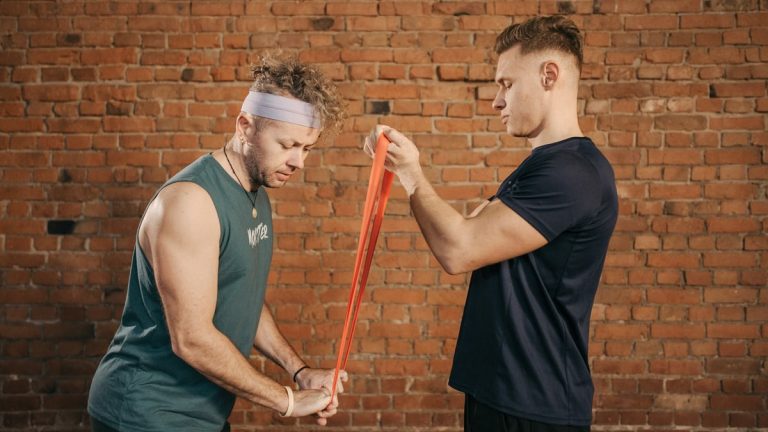 Two men engaging in a resistance band workout in a brick-walled gym setting.